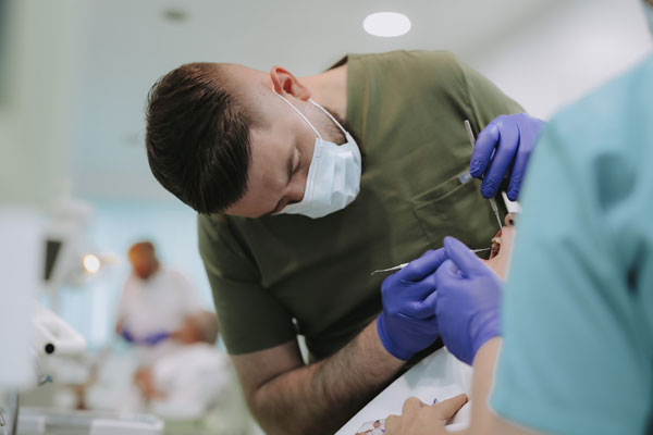 Dr Nenad Davidović, stomatolog sa maskom i u zelenoj uniformi, vr&scaron;i stomatolo&scaron;ki pregled pacijenta