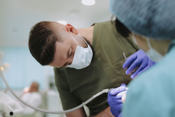 Dr Nenad Davidović, stomatolog sa maskom i u zelenoj uniformi, vr&scaron;i stomatolo&scaron;ki pregled